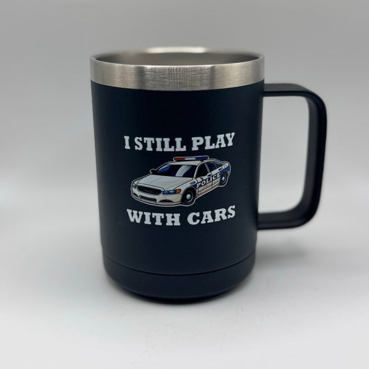 Black mug with a police car graphic and text that says I still play with cars